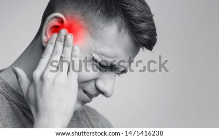 Tinnitus. Sick man having ear pain, touching his painful head, monochrome photo with red spot, free space Royalty-Free Stock Photo #1475416238