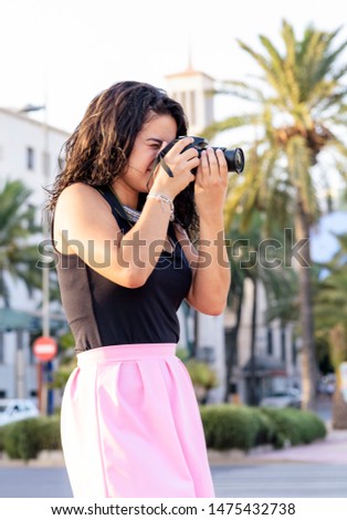 Portrait of young woman  making photos with a professional digital camera in a city.