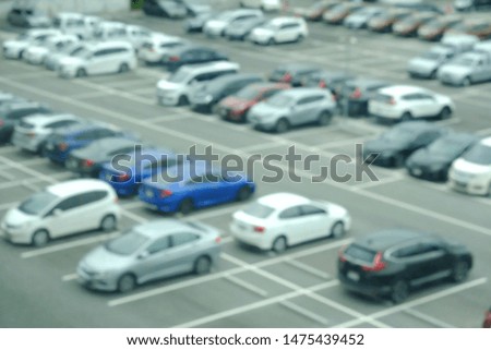 Blurred many cars in a white squares indicate parking spaces at the outdoor car park in the city ( a picture taken from a building mirror )