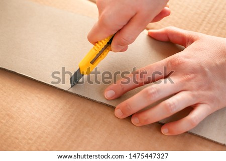 Yellow paper knife in woman hands cutting piece of cardboard. Close-up. Royalty-Free Stock Photo #1475447327