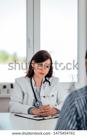 Portrait of a serious female doctor listening a patient in the medical office.