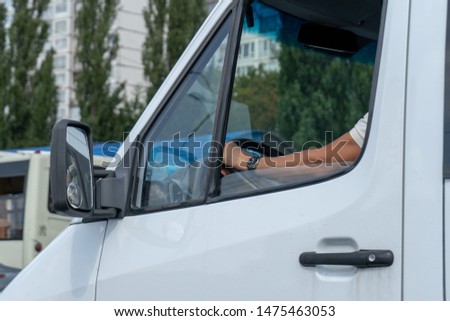 Close-up. A man (driver) sees driving a vehicle on a city road. Through the open window you can see the driver’s hand with a clock on it lies on the steering wheel