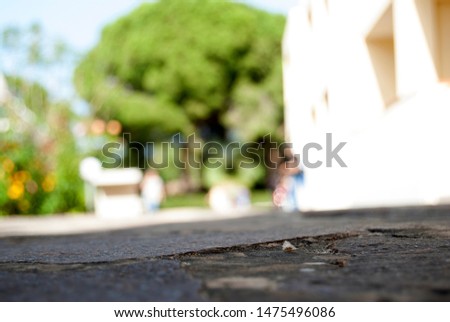 Closeup and focus on the grey stone road with bright sunny blurred yellow vacation house and green trees in the background