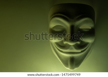 A mask that looks like a symbol of a group of hackers Anonymous. Tinted in olive color. Shooting a subject in a dark key. Background for screensaver or desktop wallpaper monitor. Close-up. Copy space.