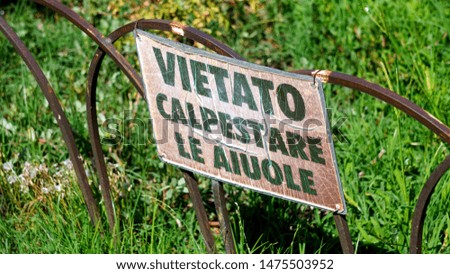 Signboard with the inscription in Italian "forbidden to step on the flowerbeds" on the railing of a public park, in the morning sun. image for urban decoration