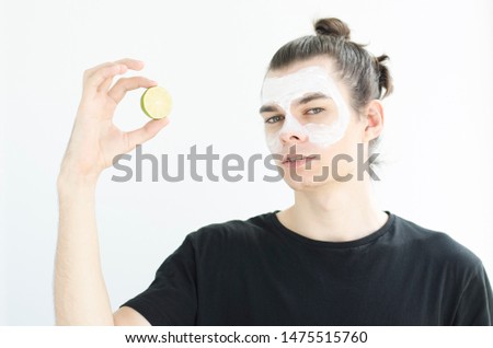 Close up beauty portrait of satisfied young man applying facial cream isolated over white background with lime.