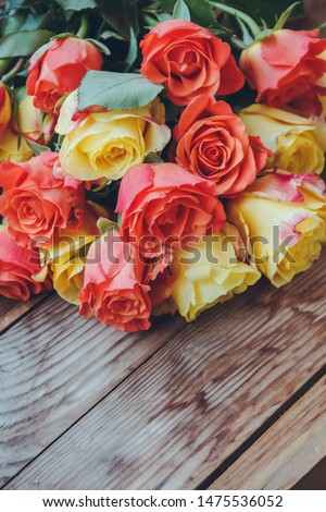 A bouquet of red and yellow roses lies on a wooden table. A lush bouquet of flowers.