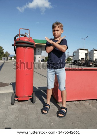 little boy stands at a gas station shows a prohibitory sign with his hands, games in such places are not allowed