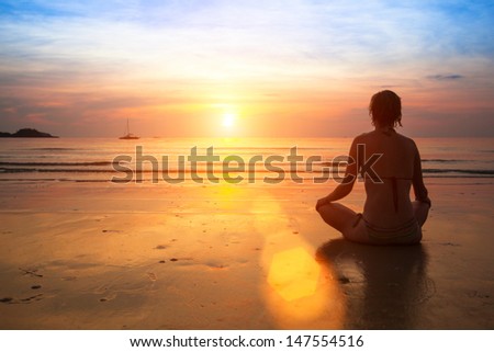 Woman practicing yoga on the ocean beach at sunset.