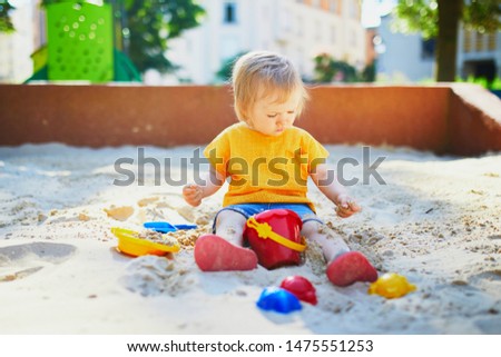 Adorable little girl having fun on playground in sandpit. Toddler playing with sand molds and making mudpies. Outdoor creative activities for kids