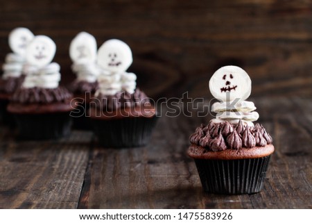 Creative concept of skeleton made from white chocolate pretzels and marshmallows over a dark chocolate cupcake. Selective focus on one in front with blurred background.