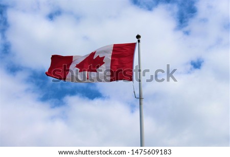 Canada flag waving in the wind against white cloudy blue sky together; Canada day celebrations; proud Canadian
