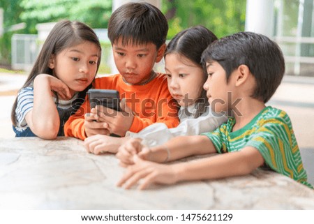 group of asian kids play game on smartphone together, smiling small brother and sister have fun hold using cellphone, watch funny cartoon. Children and technology concept