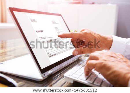 Close-up Of A Businessperson's Hand Analyzing Invoice On Laptop At Workplace Royalty-Free Stock Photo #1475631512