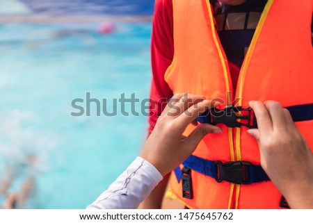 Asian mother helping her son to wear life jacket before playing in swimming pool, Selective focus. Royalty-Free Stock Photo #1475645762