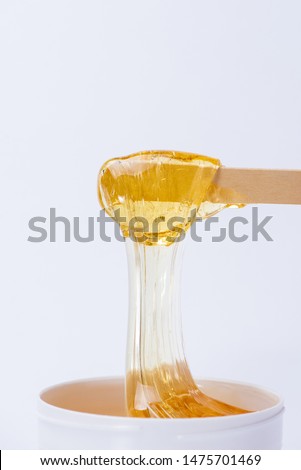 Liquid yellow sugar paste or wax for depilation on a wooden stick close-up on a white background Royalty-Free Stock Photo #1475701469