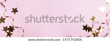 Golden decor star shaped confetti and ribbons isolated on pastel pink background. Festive party banner