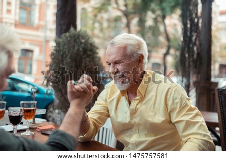 Man winning. Bearded grey-haired man laughing while winning at arm-wrestling