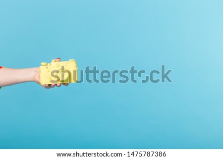 Photographing and vintage concept - female hand with yellow retro camera on blue background with copy space