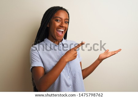 Young african american woman wearing striped shirt standing over isolated white background amazed and smiling to the camera while presenting with hand and pointing with finger.
