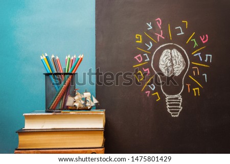 Book, pencils and light bulb with human brain and Hebrew letters on chalkboard