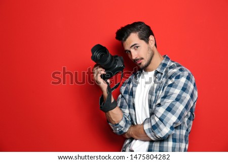 Young photographer with professional camera on red background. Space for text