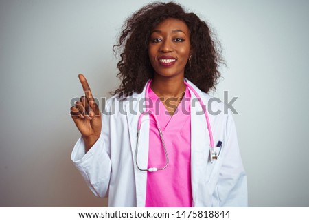 African american doctor woman wearing  pink stethoscope over isolated white background showing and pointing up with finger number one while smiling confident and happy.