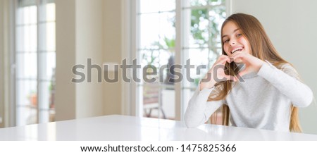 Wide angle picture of beautiful young girl kid wearing casual sweater smiling in love showing heart symbol and shape with hands. Romantic concept.