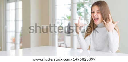 Wide angle picture of beautiful young girl kid wearing casual sweater shouting with crazy expression doing rock symbol with hands up. Music star. Heavy concept.