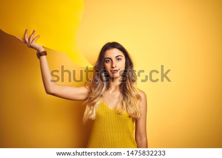Young beautiful woman holding speech bubble over yellow isolated background with a confident expression on smart face thinking serious