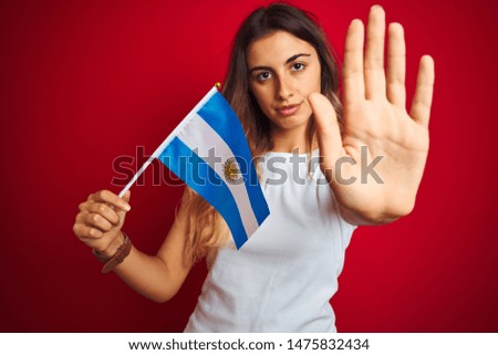 Young beautiful woman holding argentine flag over red isolated background with open hand doing stop sign with serious and confident expression, defense gesture