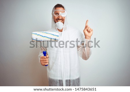 Painter man wearing professional worker equipment holding roller over isolated background very happy pointing with hand and finger to the side