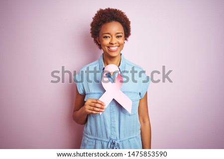 Young african american woman holding brest cancer ribbon over isolated pink background with a happy face standing and smiling with a confident smile showing teeth Royalty-Free Stock Photo #1475853590