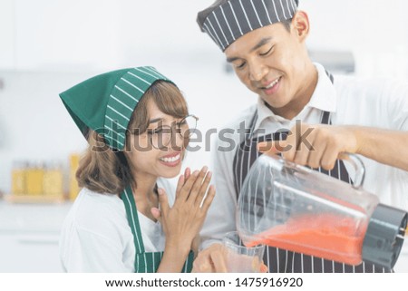 Attactive young asian couple make strawberry smoothie together in white kitchen