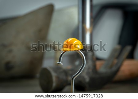Construction nail shaped as question mark with yellow plastic workplace helmet and blurred background of various construction tools, construction questions, confusion and work safety concept