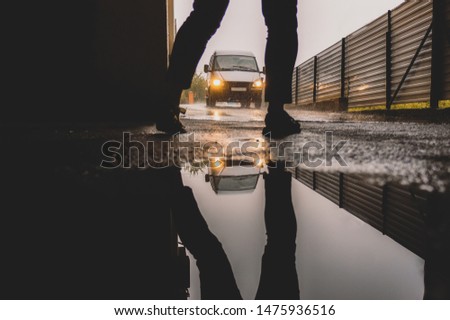 In the foreground is a girl who steps over a car that rides away. Reflection in the puddles of this picture.