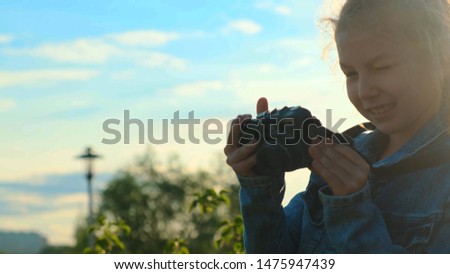 Portrait of a little girl holding a camera in her hands. She takes pictures and smiles, looks at the camera.