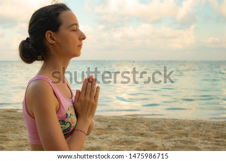 Namaste mudra. Close up. Yoga at the beach. Young woman meditating, practicing yoga and pranayama with namaste mudra. Sunset at the beach. Yoga lifestyle. Side View. Yoga retreat in Bali. Copy space.