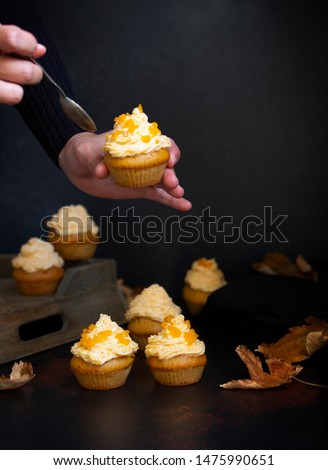 Pumpkin cupcakes on a dark backgroun. Female hand holding cupcake. Autumn background pumpkins and leaves. Pumpkin sweets. Halloween and Thanksgiving sweets. Selective focus. Copyspace. Vertical