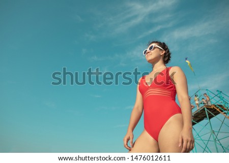 woman in red swimsuit in white sunglasses blue sky on background copy space looking forward
