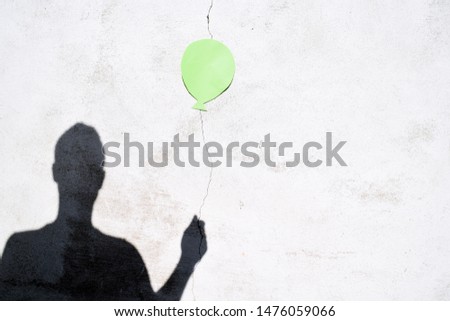 A crack has been created on a white wall, a piece of paper in the form of a balloon has been hung up and the shadow of a person holding the balloon at the crack - concept with shadow