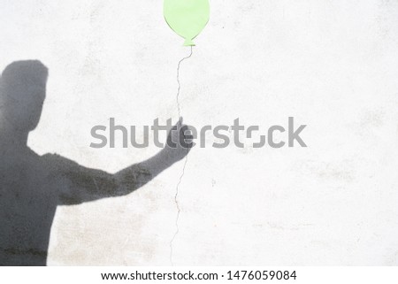 A crack has been created on a white wall, a piece of paper in the form of a balloon has been hung up and the shadow of a person holding the balloon at the crack - concept with shadow