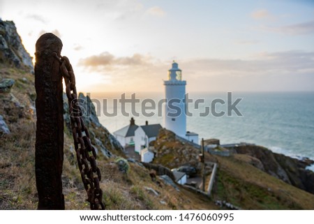 Picture of a climbing fencing rusted chain with blurred lighthouse in the background during sunrise