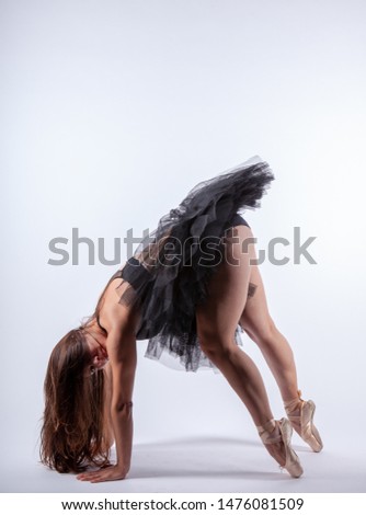 Young beautiful pregnant ballerina with black dress is posing in studio.