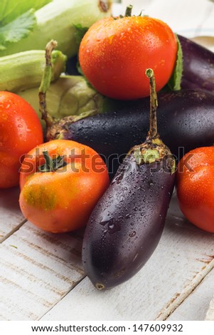 Fresh ripe tomatoes, eggplants, marrows on white wooden background. Selective focus. Rustic style.