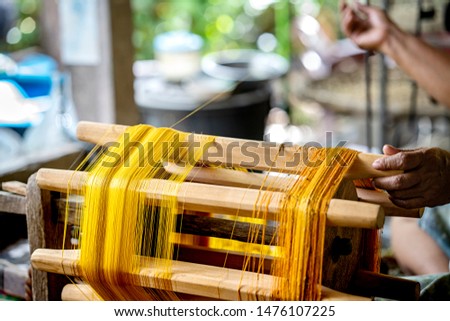 Crafts and craftsmanship. Silk raising for silk threads. yarn warping machine in a textile weaving crafsmanship. Hand of woman weaving and spinning natural colorful threads or yarn. Royalty-Free Stock Photo #1476107225
