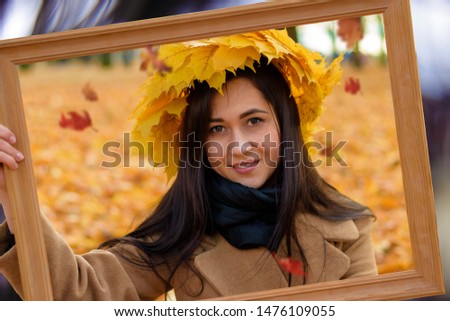 Joyful pretty young happy woman with a beautiful smile in an elegant coat with a bouquet of autumn leaves on her head poses in a park. The cheerful girl walks in the fresh air. Great weekend. Season.