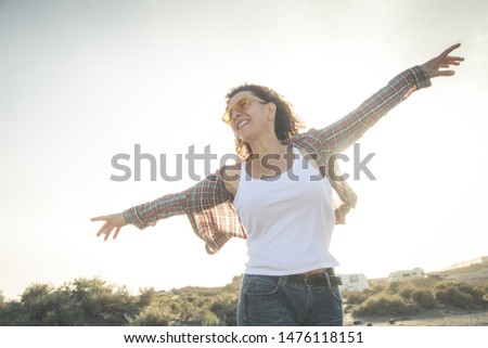 Trendy woman dancing with open arms on the beach in a beautiful summer evening. Smiling tourist girl enjoy freedom alone during estival holidays. Feminine, carefree, happiness and fun concept.