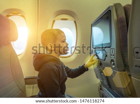 Adorable little boy traveling by airplane. Child sitting by aircraft window and looking on monitor. Traveling abroad with kids.