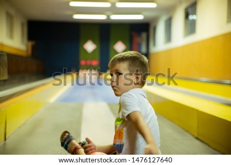 A little boy pictured from behind is sitting in a bowling alley
